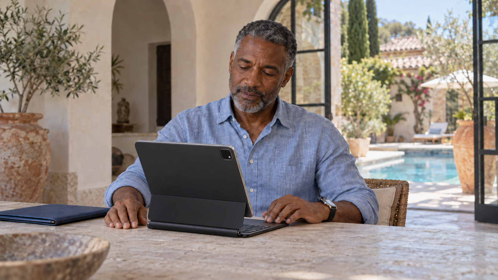 A man pauses beside an iPad Pro attached to a Magic Keyboard at a table in a villa.